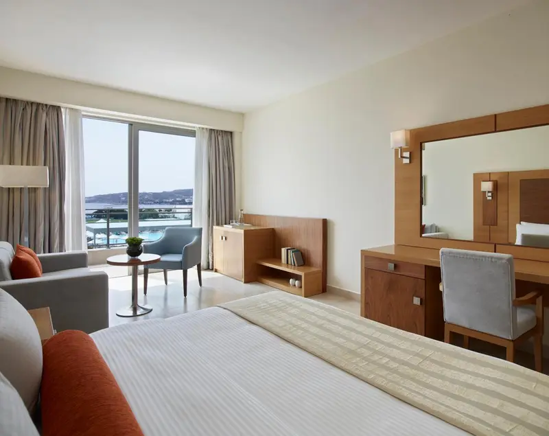 Chambre lumineuse avec un canapé, une table basse et un bureau près d'une grande fenêtre.