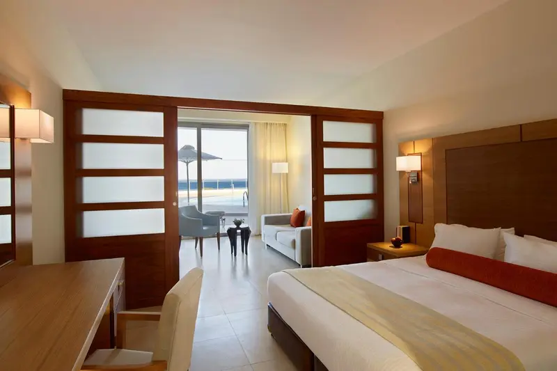 Une chambre lumineuse avec un lit et un espace salon ouvert sur une vue extérieure.