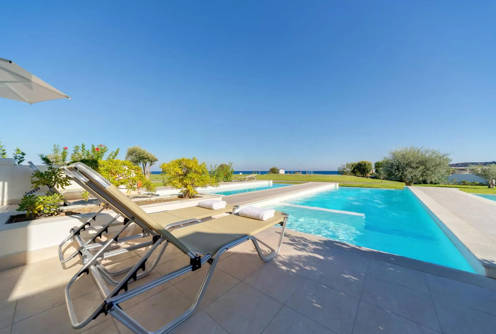 Transats alignés au bord d'une piscine turquoise avec vue sur la mer.