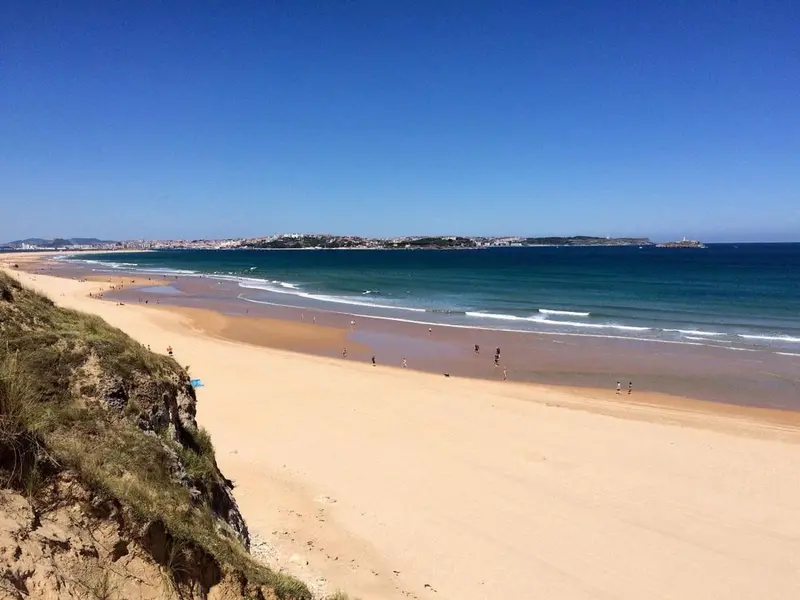 Une longue plage de sable fin bordée d'une eau turquoise sous un ciel bleu dégagé.