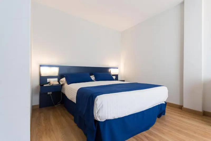 Une chambre avec un grand lit recouvert d'une couette blanche et bleue.