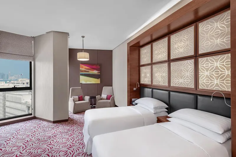 Chambre moderne avec deux lits et fauteuils près d'une fenêtre.