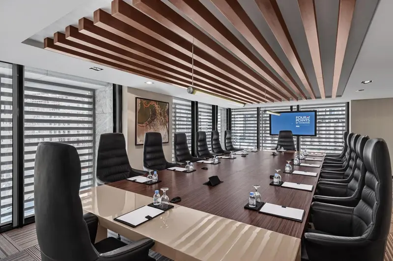 Une longue table de réunion est entourée de chaises en cuir noir dans une salle lumineuse.