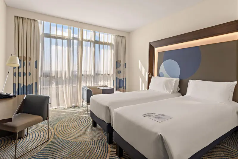 Chambre d'hôtel lumineuse avec deux lits simples et vue sur la mer.