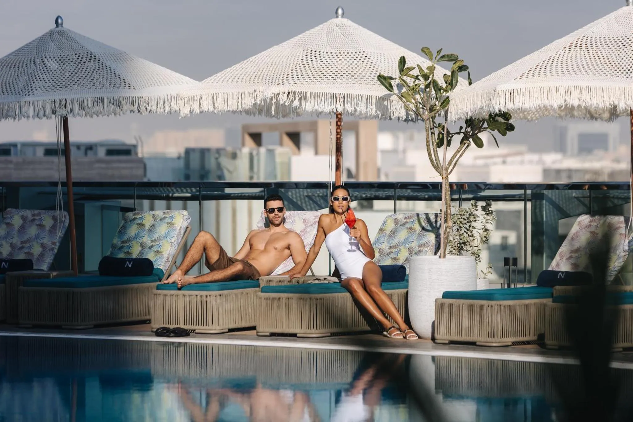 Deux personnes se détendent sur des transats au bord d'une piscine ensoleillée.