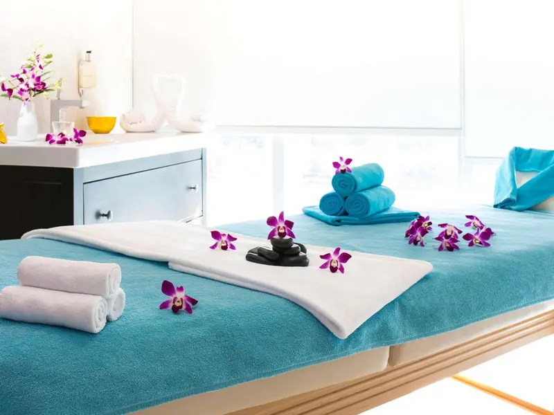 Table de massage recouverte d'une serviette turquoise, décorée de fleurs et de pierres.