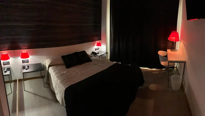 Une chambre moderne avec un lit recouvert d'une couverture sombre et des lampes rouges.
