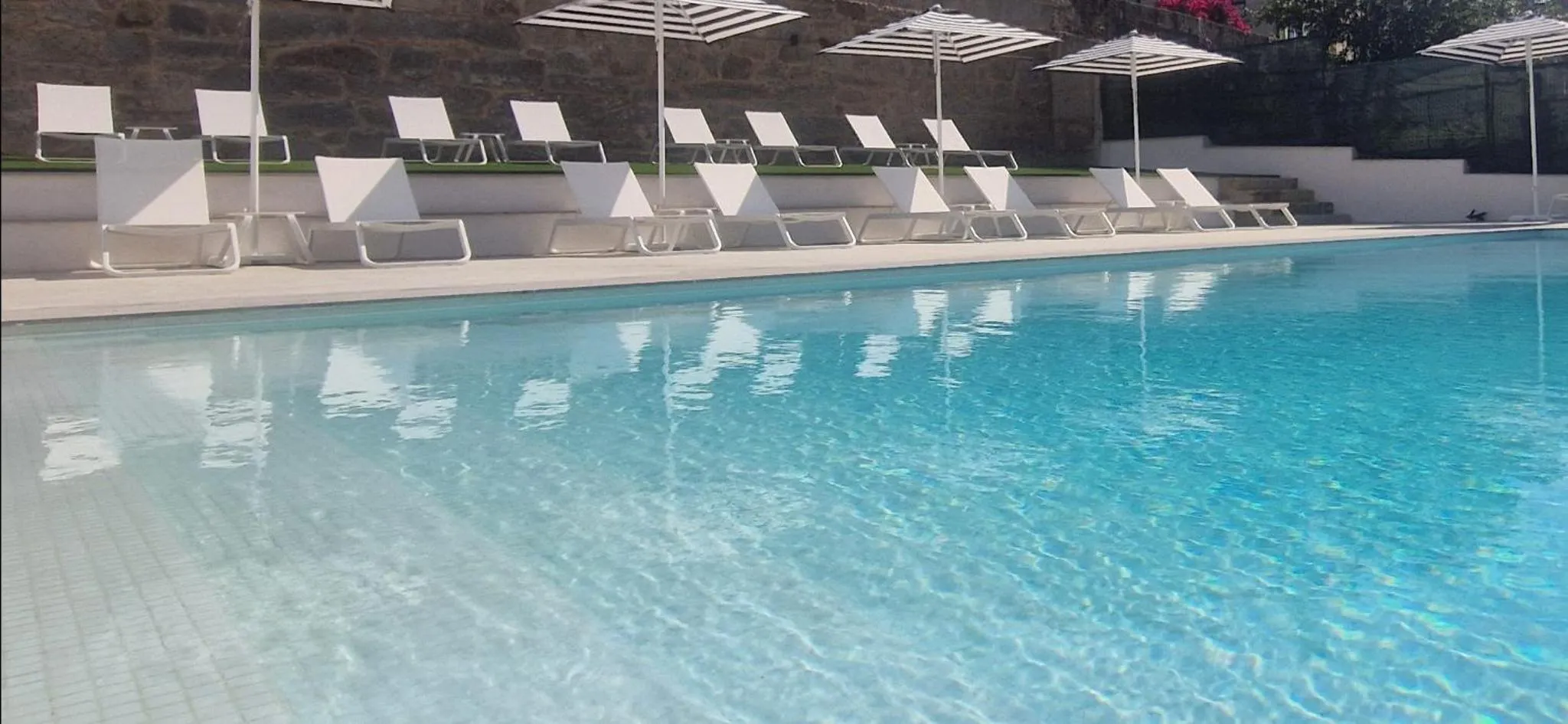 Transats blancs alignés au bord d'une piscine turquoise.