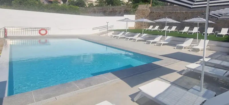 Une piscine rectangulaire avec des transats blancs et des parasols rayés.