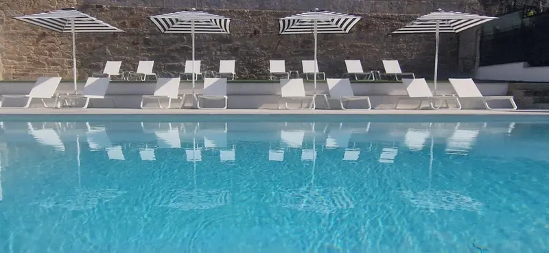 Transats blancs alignés au bord d'une piscine rectangulaire turquoise.