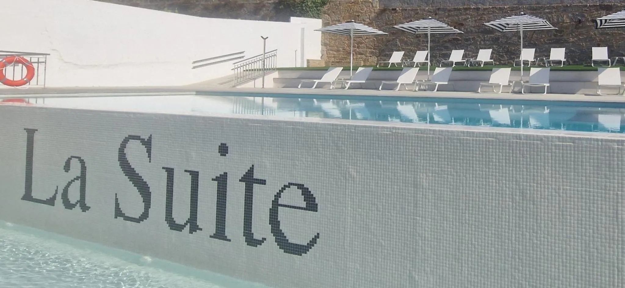 Une piscine rectangulaire avec des transats blancs alignés sur une terrasse.