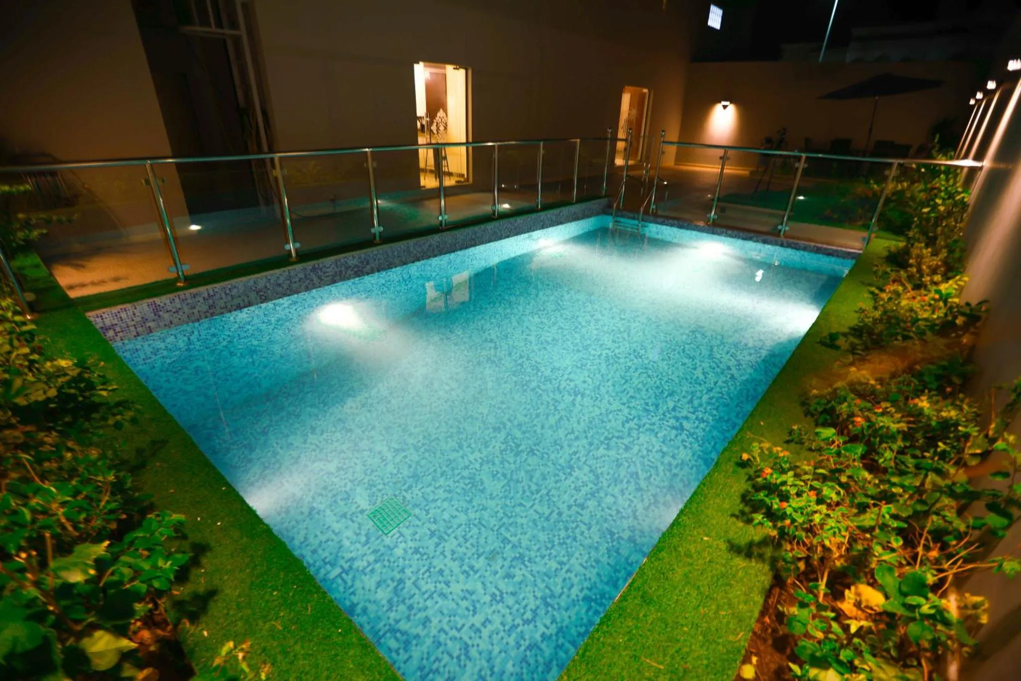 Une piscine rectangulaire illuminée au crépuscule, entourée de verdure et d'une balustrade.