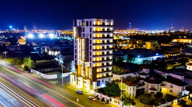 Bâtiment moderne illuminé la nuit avec une route passante en contrebas.