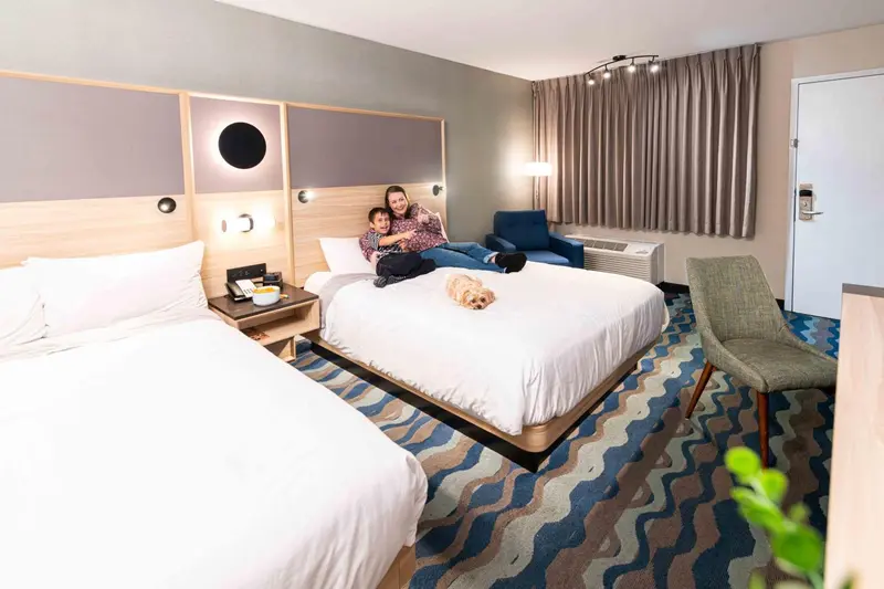 Une chambre d'hôtel lumineuse avec deux lits et un couple assis dessus.