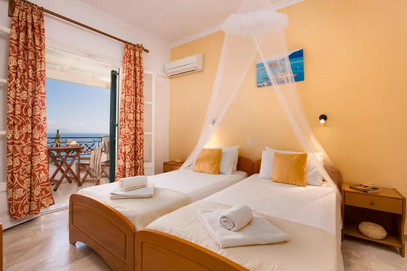 Chambre lumineuse avec deux lits et balcon donnant sur la mer.