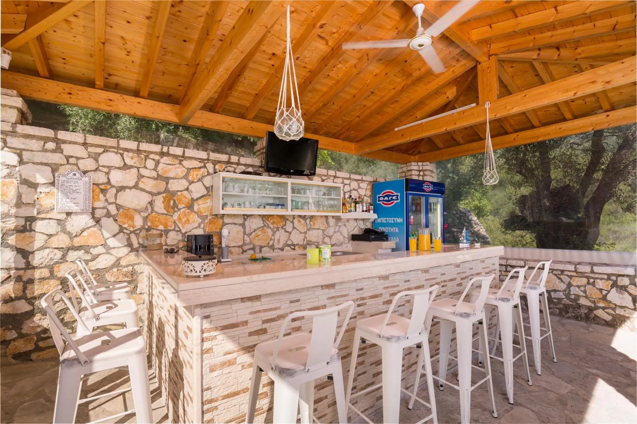 Un comptoir de bar en plein air avec des tabourets blancs et une décoration murale en pierre.