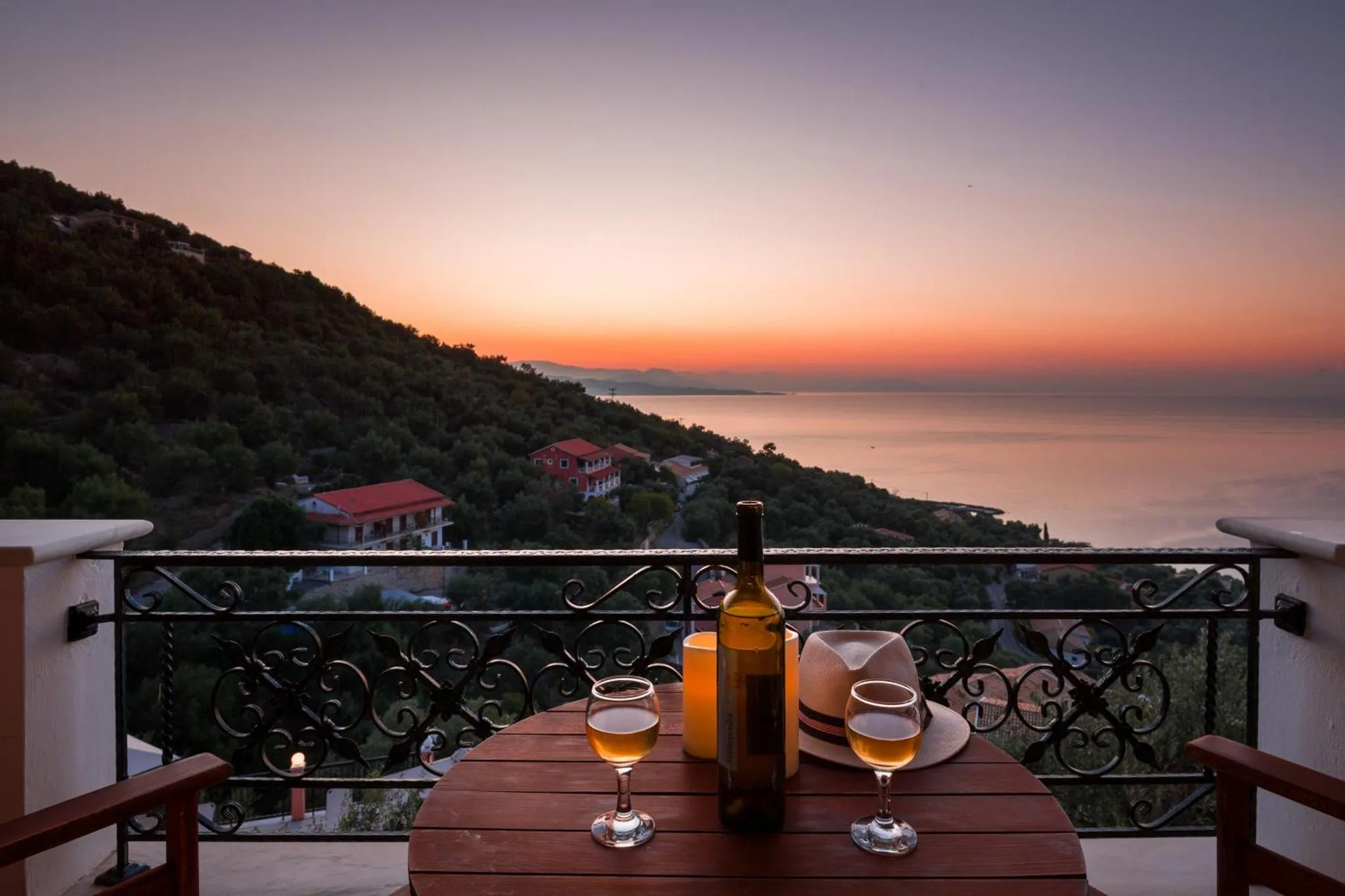 Une table avec des verres de vin est placée sur une terrasse avec vue sur la mer au coucher du soleil.