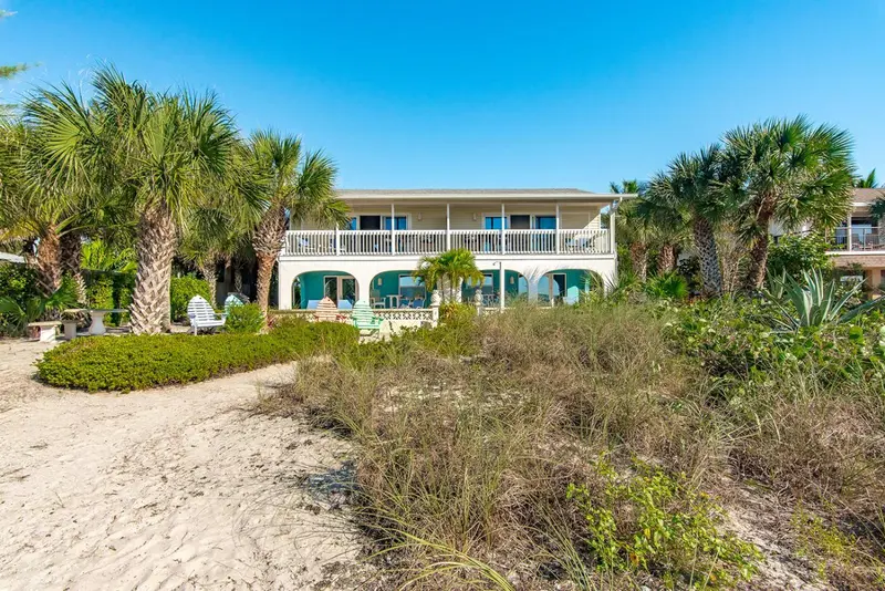 Bâtiment blanc avec des palmiers et une végétation luxuriante sur une plage de sable.