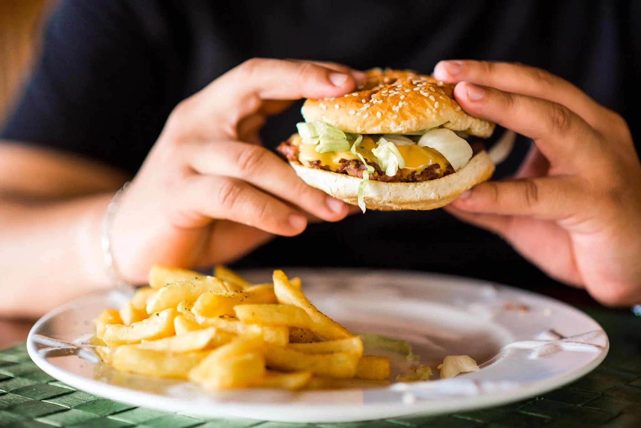 Un homme tient un hamburger au-dessus d'une assiette de frites.
