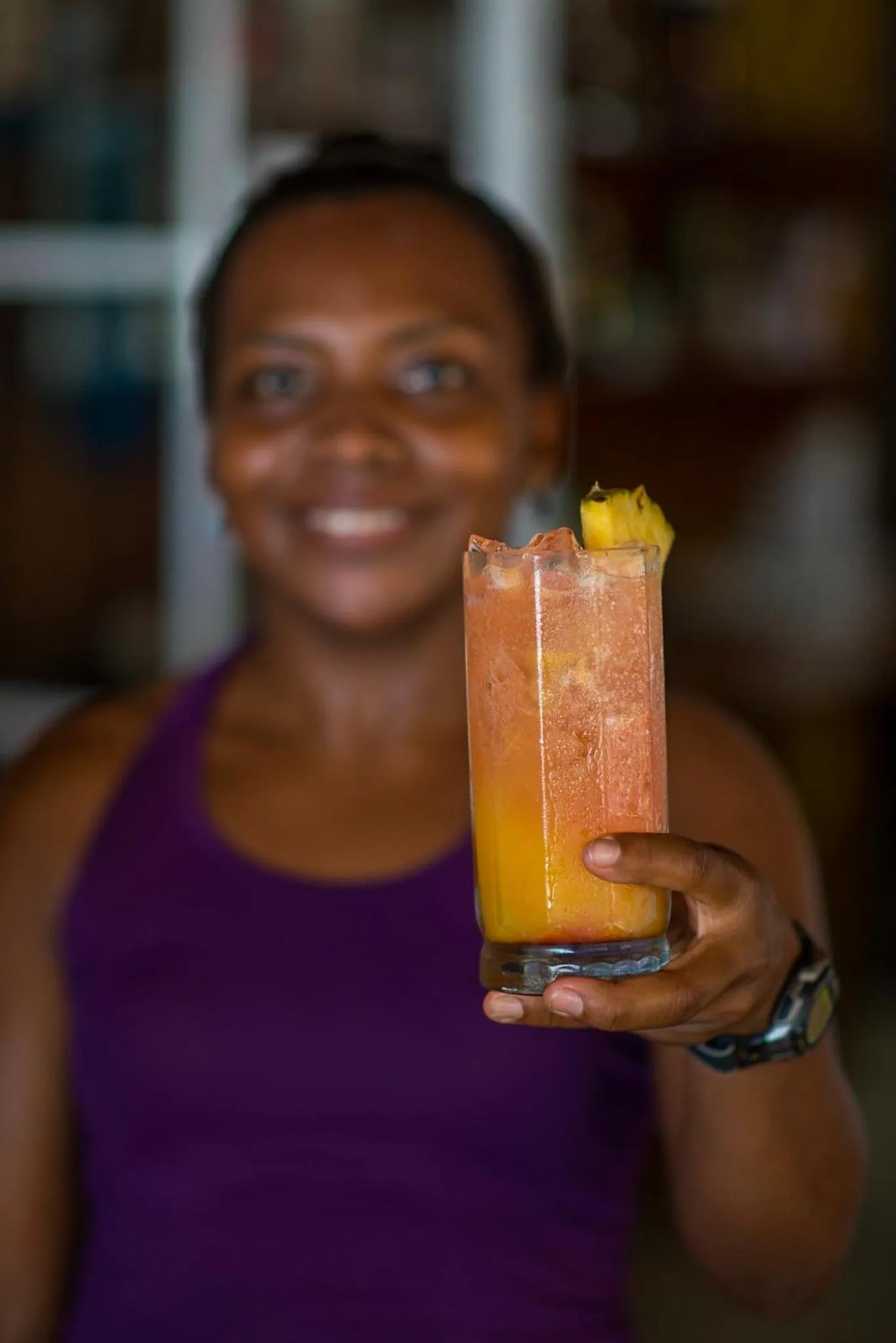 Une femme souriante tient un cocktail coloré devant elle.