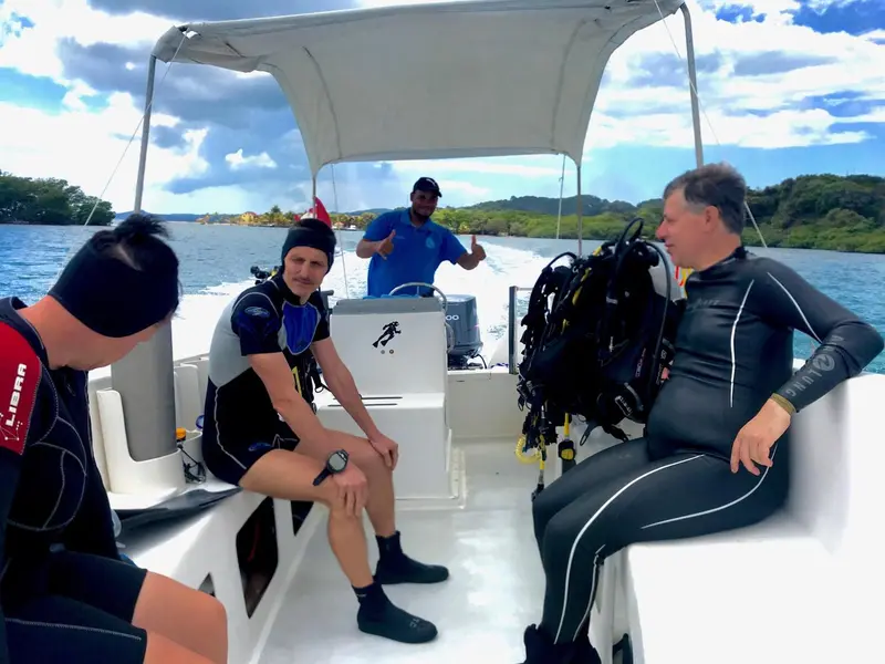 Trois personnes en combinaison de plongée sont assises dans un bateau blanc.