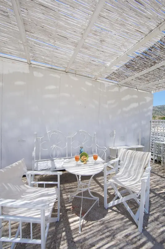 Une table et des chaises blanches sont disposées sous une pergola claire.