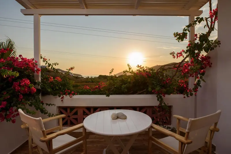 Terrasse avec table et chaises donnant sur un coucher de soleil en mer.