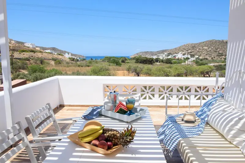 Une table avec des fruits et des boissons est mise en scène sur une terrasse ensoleillée.