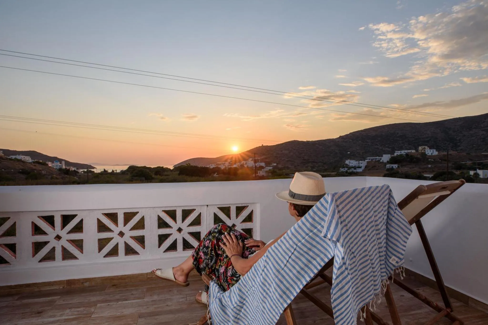 Une personne se détend sur une chaise longue sur une terrasse avec vue sur un paysage montagneux au coucher du soleil.