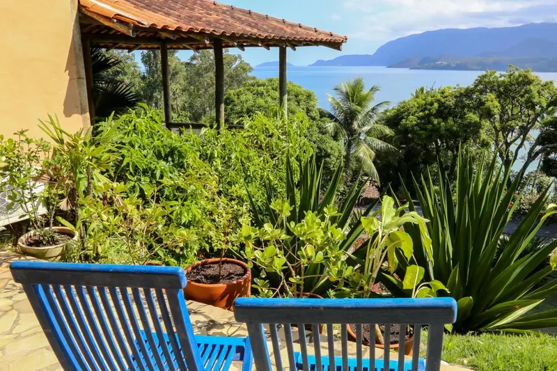Deux fauteuils bleus sont placés devant une végétation luxuriante avec vue sur la mer.