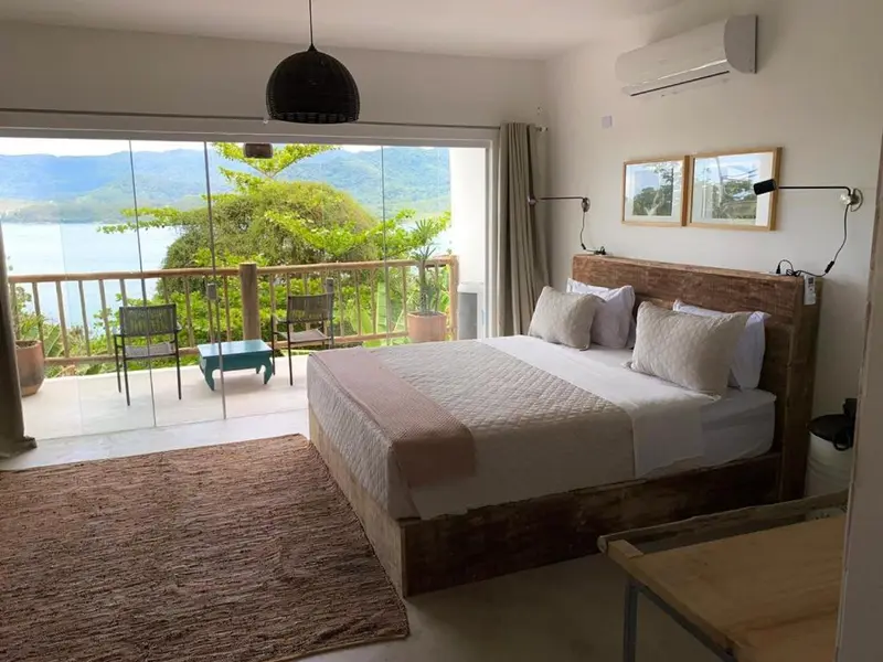 Une chambre lumineuse s'ouvre sur une terrasse avec vue sur la mer et les montagnes.