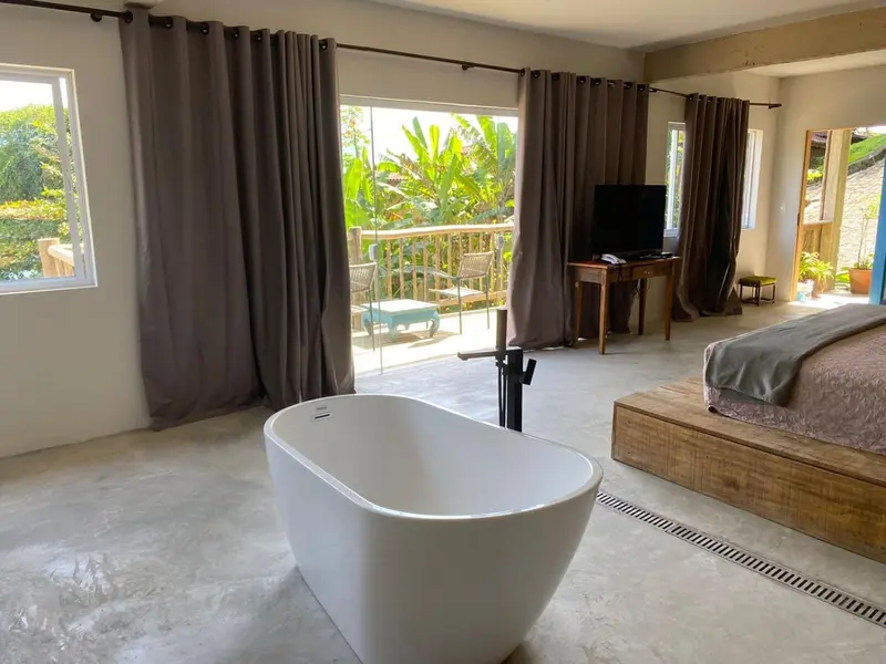 Une chambre lumineuse avec baignoire et accès à une terrasse verdoyante.