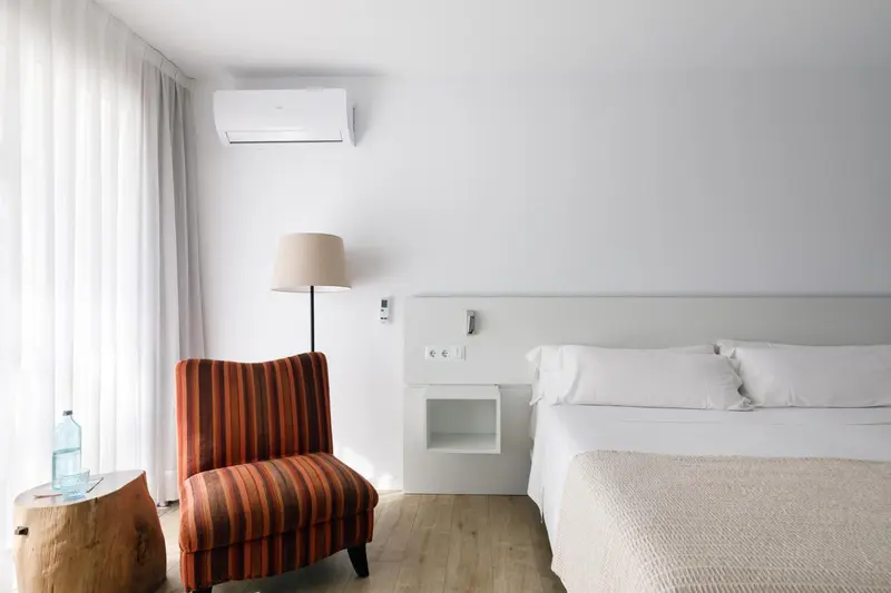 Une chambre lumineuse avec un fauteuil coloré et un lit blanc.