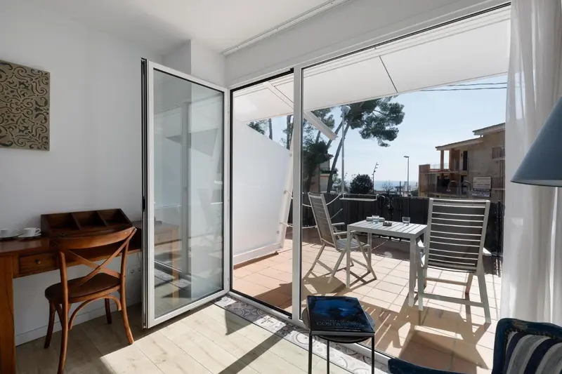Une pièce lumineuse s'ouvre sur une terrasse ensoleillée avec vue sur la végétation.