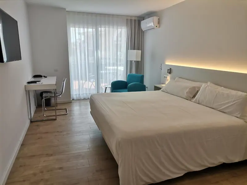 Chambre lumineuse avec un grand lit et un espace bureau.