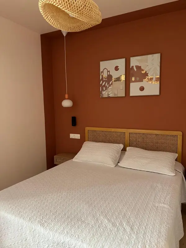 Une chambre lumineuse avec un lit recouvert d'une courtepointe blanche et des tableaux décoratifs au mur.