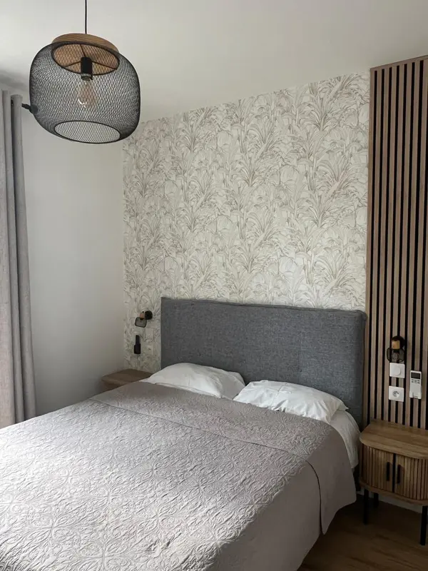 Une chambre à coucher avec un lit recouvert d'une couverture texturée et un mur décoré de motifs végétaux.