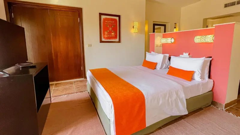 Une chambre lumineuse avec un grand lit recouvert d'une courtepointe orange et de coussins.