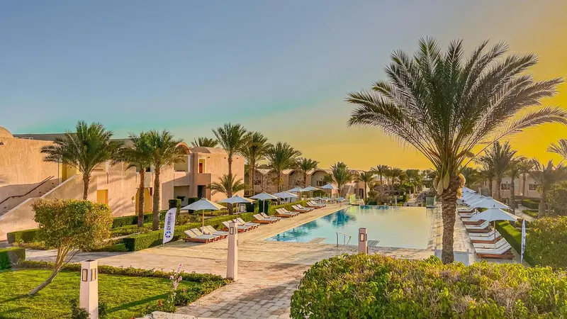 Vue d'un complexe hôtelier avec piscine et palmiers au coucher du soleil.