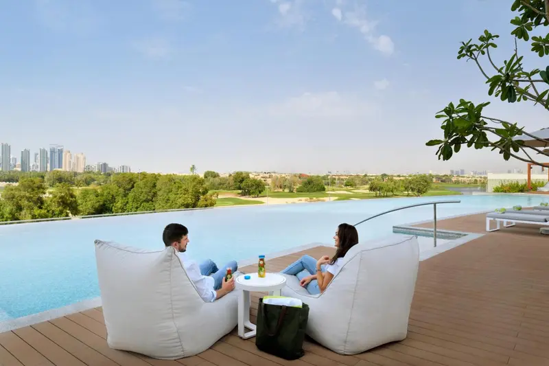 Deux personnes se détendent sur des fauteuils blancs au bord d'une piscine à débordement avec vue sur un paysage urbain.