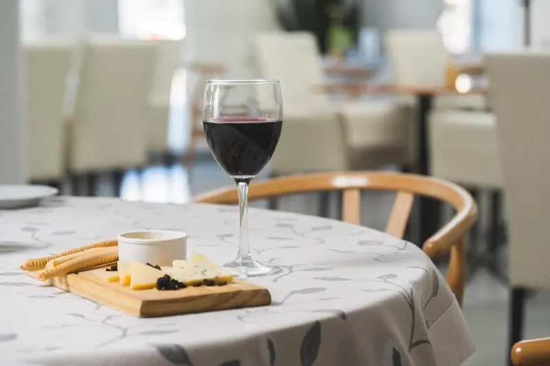 Un verre de vin rouge et une assiette de fromage sont posés sur une table nappée.