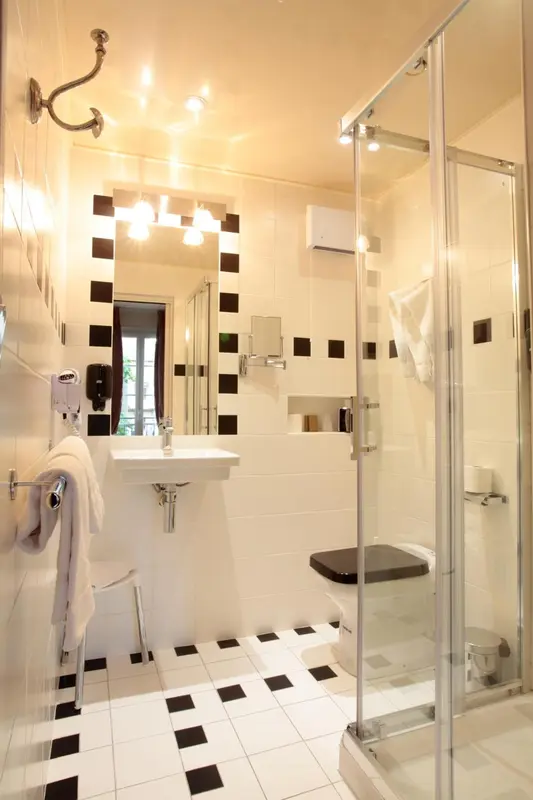 Une salle de bain carreee avec douche a l'italienne et carrelage noir et blanc.