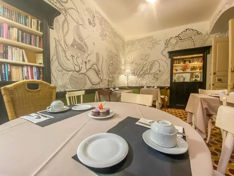 Une table ronde est dressée avec de la vaisselle et des pâtisseries dans une salle lumineuse.