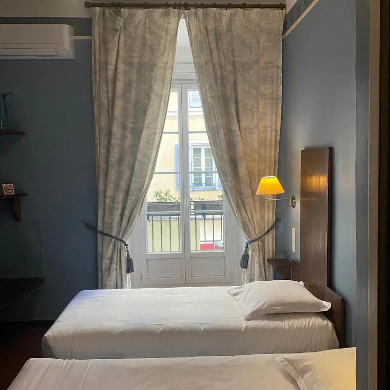 Une chambre lumineuse avec un lit simple et une fenêtre donnant sur un balcon.
