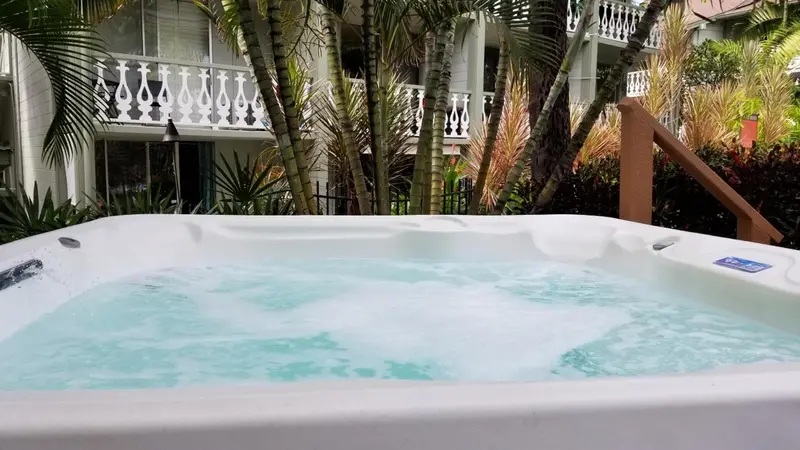 Un jacuzzi extérieur avec de l'eau turquoise et des bulles, entouré de végétation tropicale et d'un bâtiment.