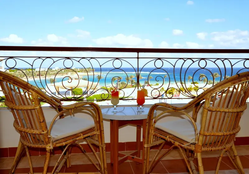 Deux fauteuils en osier et une table avec des boissons sur une terrasse ensoleillée avec vue sur la mer.