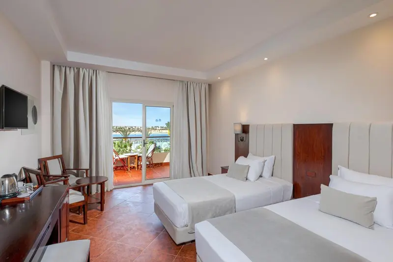Chambre lumineuse avec deux lits et vue sur la mer depuis un balcon.
