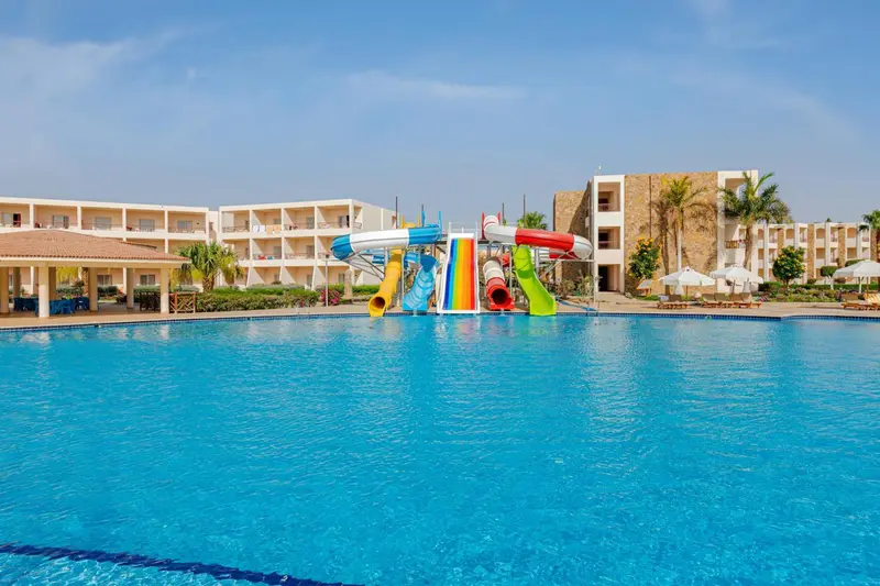 Une piscine turquoise avec des toboggans colorés et des bâtiments en arrière-plan.
