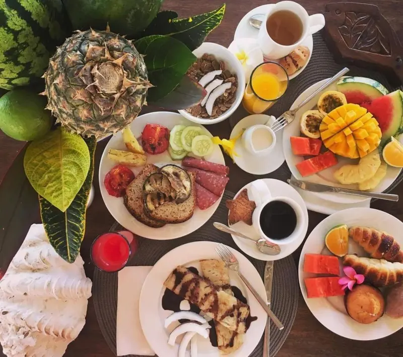 Une table est dressée avec des fruits frais, des viennoiseries et des boissons.