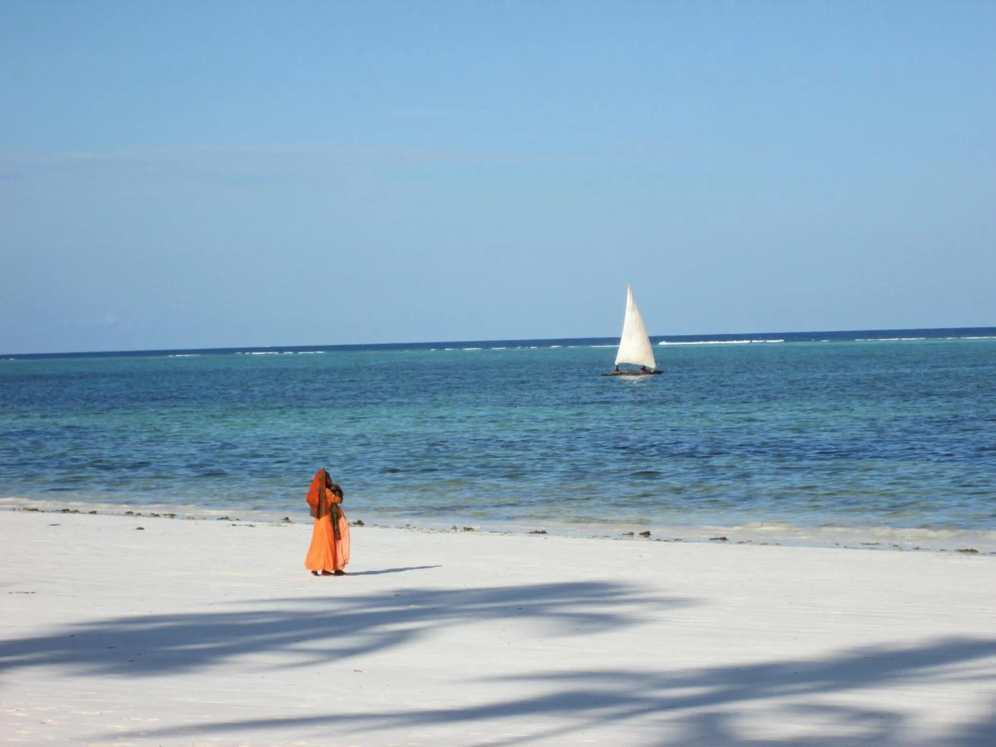 Une personne se tient sur une plage de sable blanc face à la mer.